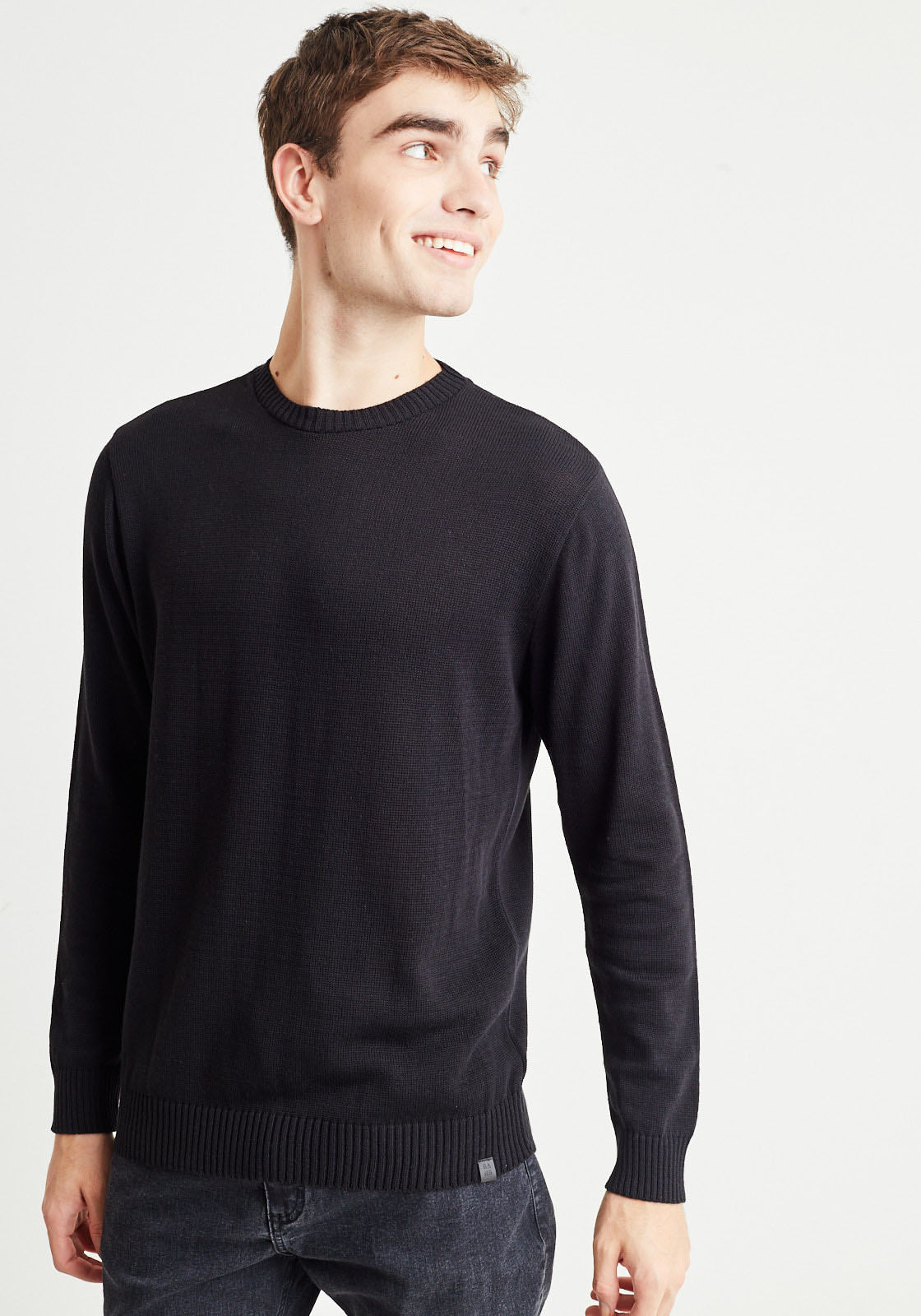 homem veste blusão de tricot preto com gola redonda e calça jeans de lavagem escura